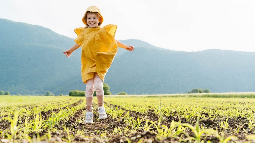 Ein Mädchen in gelbem Kleid hüpft auf einem Feld
