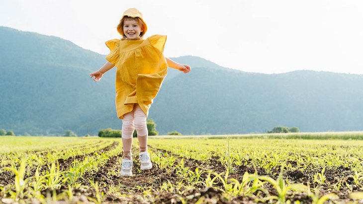Ein Mädchen in gelbem Kleid hüpft auf einem Feld
